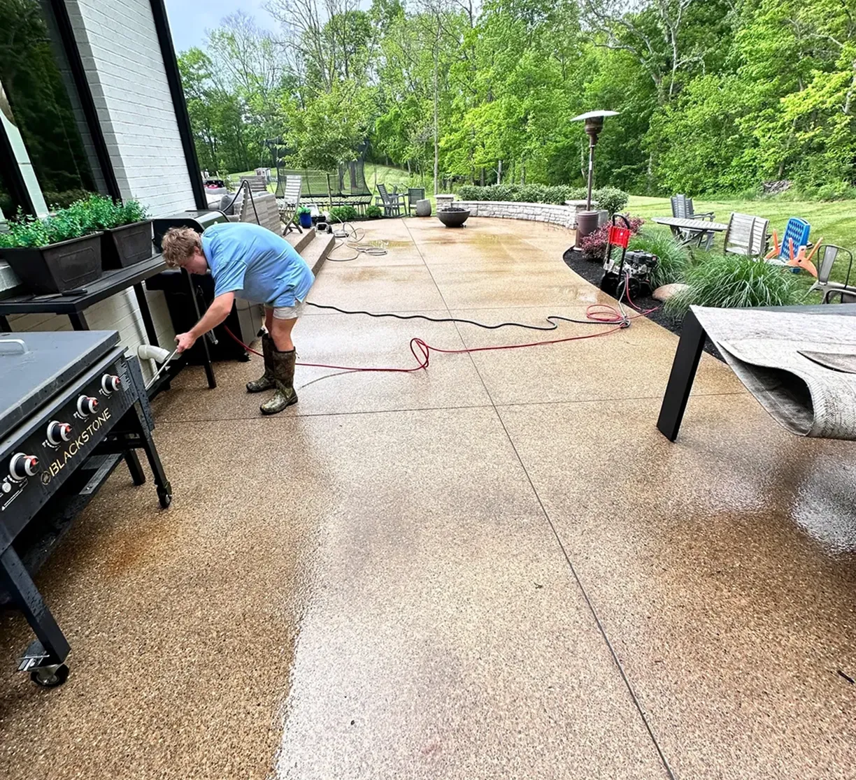 Person cleaning outdoor patio with hose.