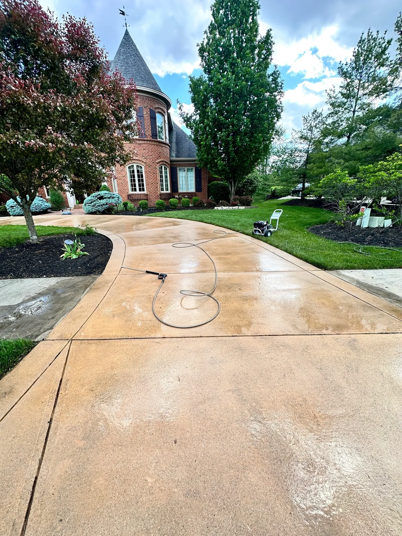 Wet driveway with hose near brick house.
