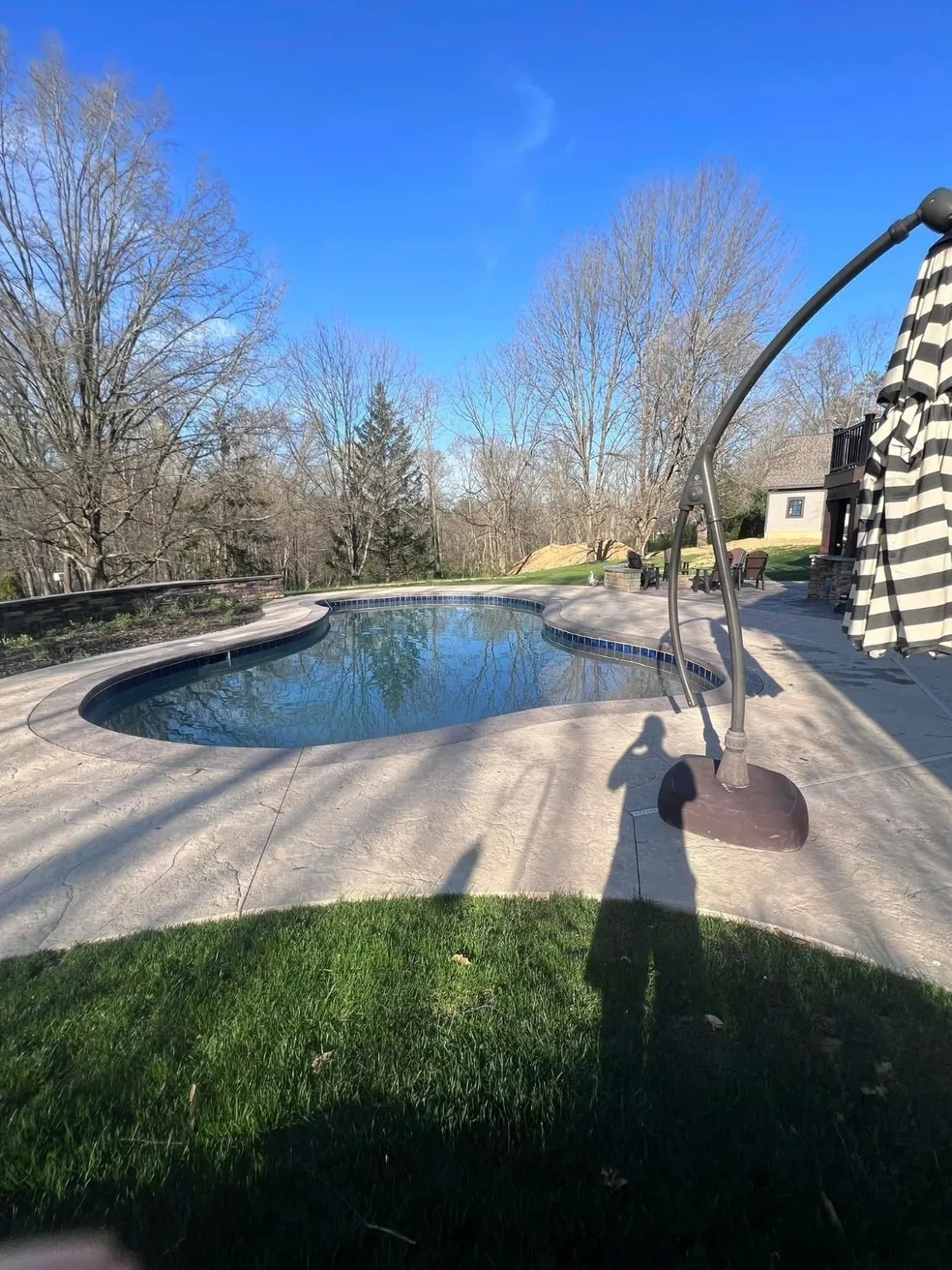 Backyard pool with surrounding trees and umbrella.